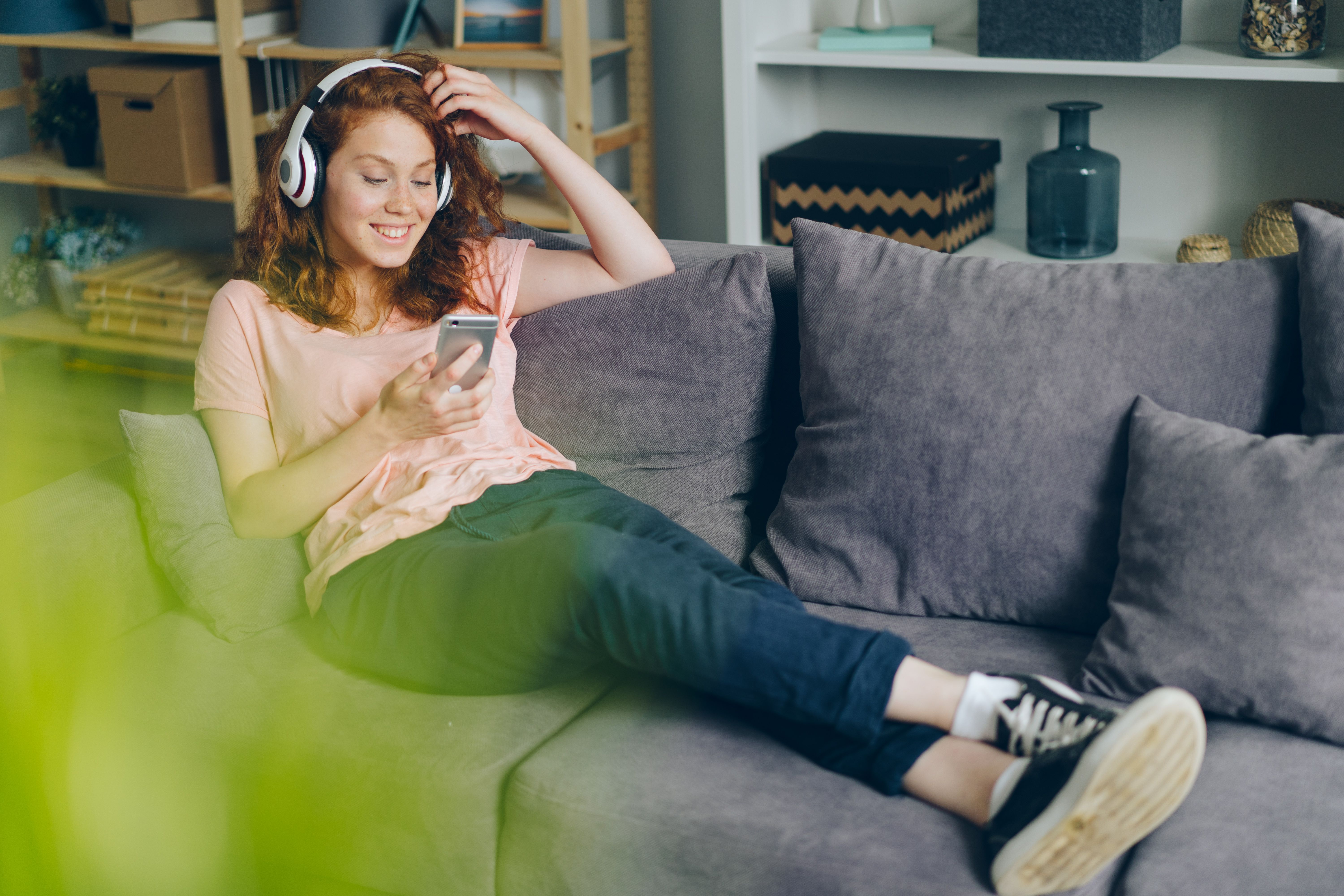 Une jeune femme avec un casque audio, allongée sur un canapé